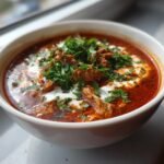 A bowl of Blitzschnelle Gyrossuppe, featuring meat, a creamy swirl, and fresh herbs.