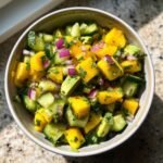 Bowl of Blitzschneller Mango-Gurken-Salat mit Avocado, featuring mango, cucumber, avocado, and red onion.