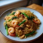 Close-up of Gebratene Glasnudeln mit Garnelen, featuring glass noodles, shrimp, green vegetables, and cashews.
