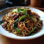 Close-up of Gebratene Nudeln mit Schweinefleisch, garnished with green onions and spinach.