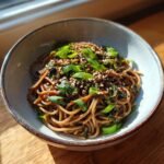 Gebratene Soba Nudeln mit Sesam, serviert in einer Schüssel, garniert mit Frühlingszwiebeln und Sesamkörnern.