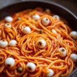 Close-up of Gruselig leckere Halloween Pasta mit Mozzarella-Augäpfeln in a pan, featuring spaghetti and mozzarella eyeballs.