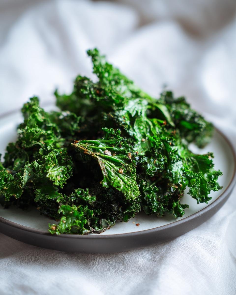 Close-up of Knusprige Grünkohl-Chips mit Knoblauch on a plate, showing their crispy texture and vibrant green color.