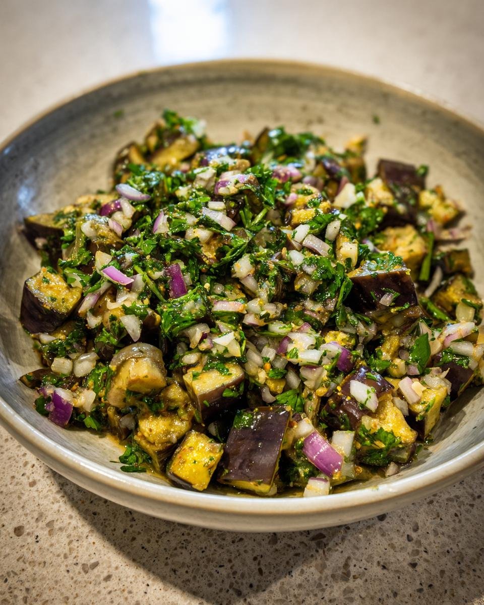 Close-up of Mediterraner Auberginen-Salat mit Petersilie, showing eggplant, red onion, and parsley in a bowl.