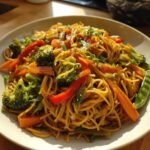 Teller mit Schnelle Chinesische Gebratene Nudeln mit Gemüse, inklusive Brokkoli, Karotten und Paprika.