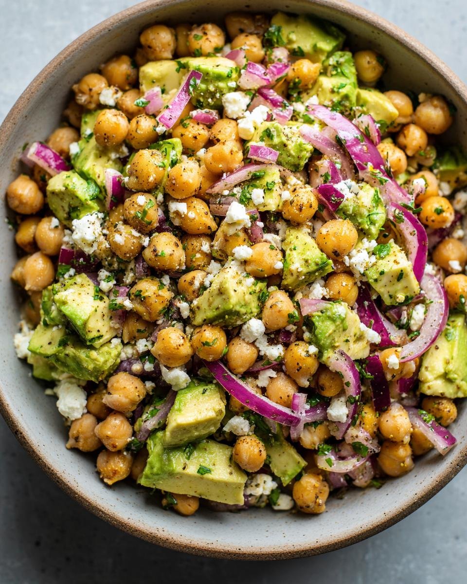 A bowl of Schneller Kichererbsen-Feta-Avocado-Salat, featuring chickpeas, feta, avocado, and red onion.