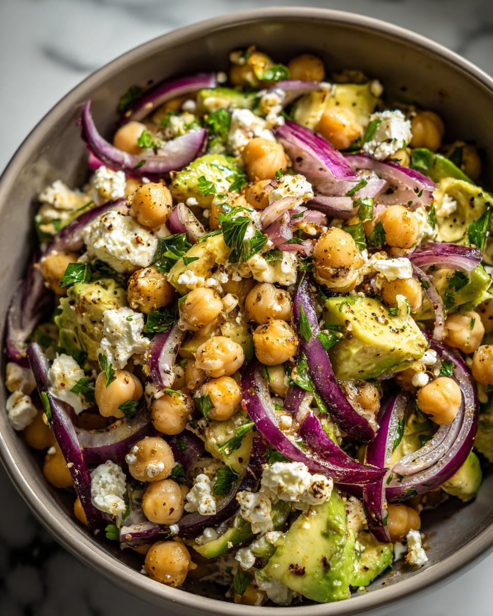 Bowl of Schneller Kichererbsen-Feta-Avocado-Salat with chickpeas, feta, avocado, and red onion.
