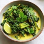 Bowl of Schnelles Grünkohl-Kokos-Curry garnished with cilantro and a lime wedge. Creamy and delicious!