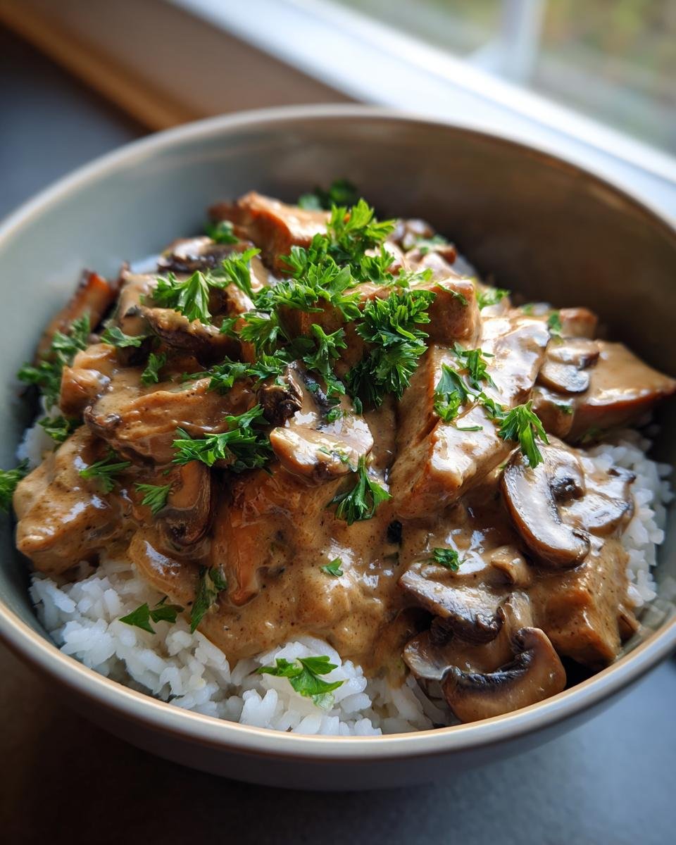 A bowl of Mushroom and Seitan Stroganoff served over rice, garnished with fresh parsley.