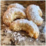 Close-up of Omas Vanillekipferl, a German vanilla crescent cookie, generously dusted with powdered sugar.