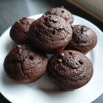 Mehrere Protein-reiche Schoko-Brötchen auf einem weißen Teller, mit Schokostückchen dekoriert.