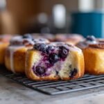 Close-up of Schnelle Heidelbeer-Quarkbrötchen with blueberries and glaze on a cooling rack.