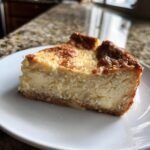 A delicious slice of Schneller Quarkkuchen, a creamy German cheesecake, on a white plate.