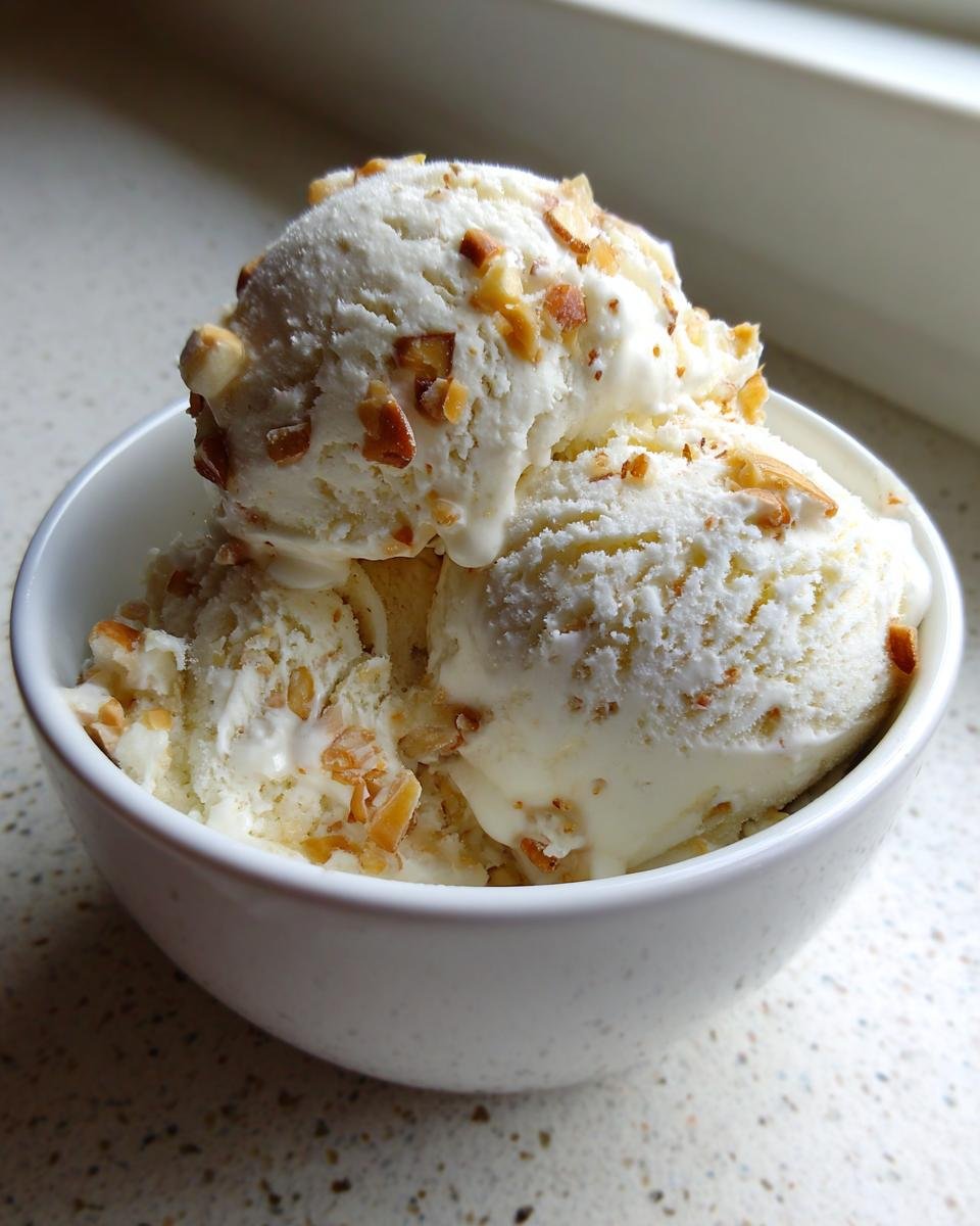 A white bowl filled with three scoops of creamy Gebrannte Mandel Eis, topped with crunchy toasted almonds.