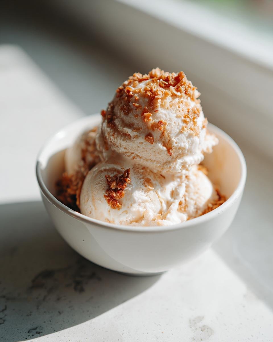 Eine Schüssel mit cremigem Gebrannte Mandel Eis, garniert mit gehackten karamellisierten Mandeln.