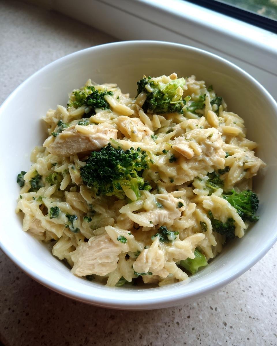 Nahaufnahme von Cremige Hähnchen-Brokkoli-Orzo mit cremiger Sauce, Hähnchenstücken und leuchtend grünen Brokkoliröschen in einer weißen Schüssel.