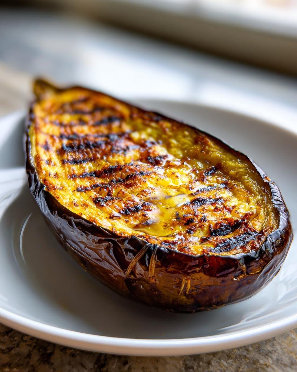 Eine perfekt gebackene Hälfte der Goldbraune Ofen-Aubergine mit deutlichen Grillspuren und glänzender Oberfläche.