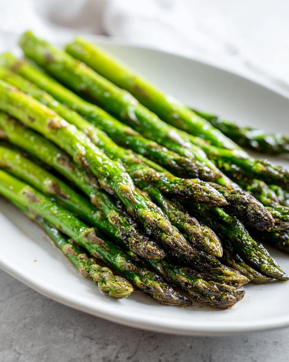 Nahaufnahme von saftigem, grünem Knuspriger Ofen-Spargel auf einem weißen Teller.