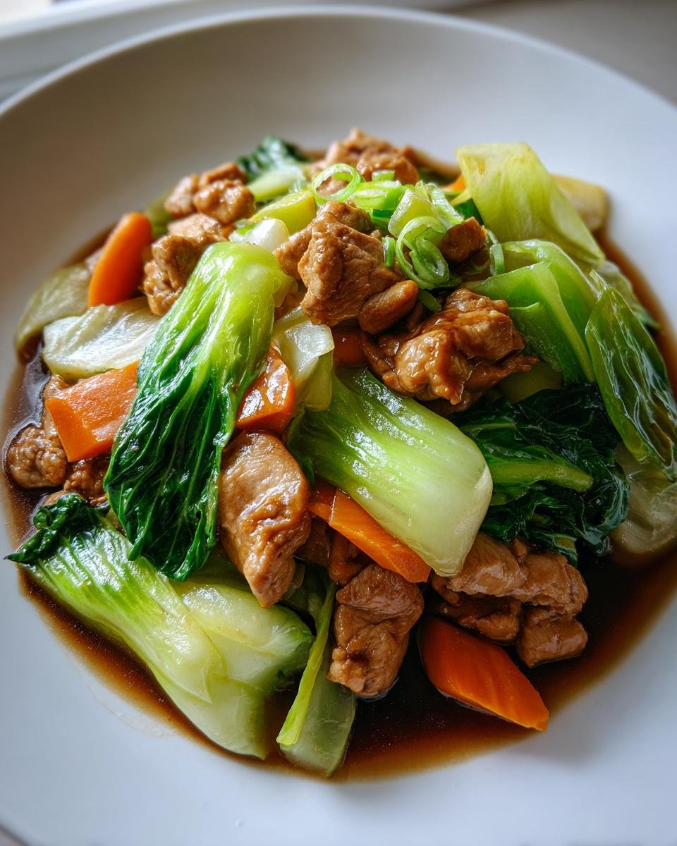 Nahaufnahme eines Köstliches Chinakohl-Pfannengericht mit saftigem Fleisch, leuchtend grünen Pak Choi Blättern und Karottenscheiben in dunkler Soße.
