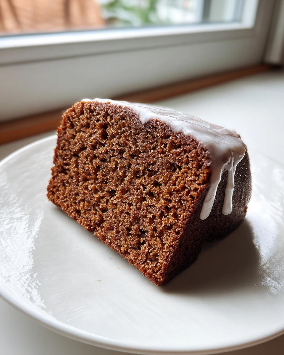 Ein Stück dunkler, saftiger GESUNDER LEBKUCHEN mit weißem Zuckerguss auf einem weißen Teller.