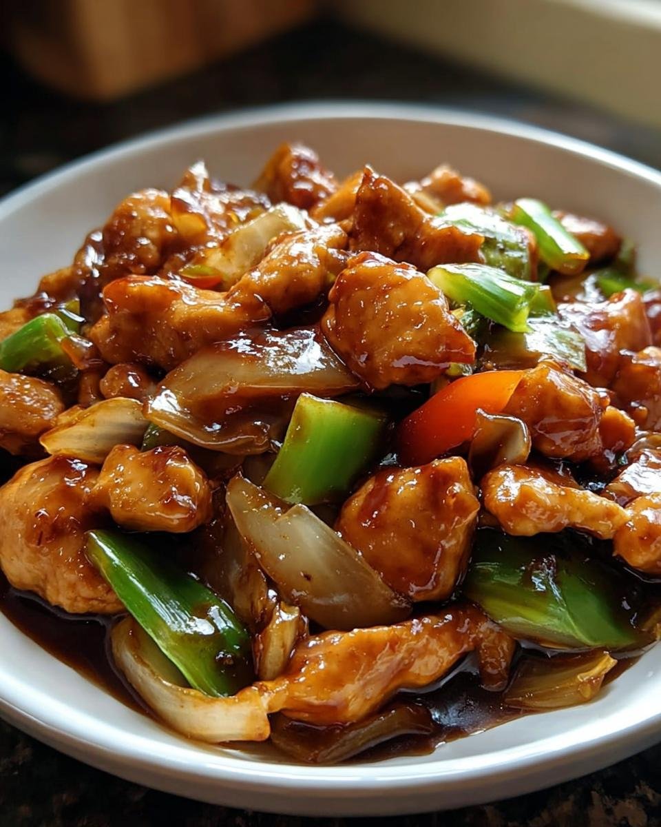 Nahaufnahme einer Chinesische Hähnchenpfanne mit Spitzkohl und Zwiebel in dunkler Soße in einer weißen Schale.