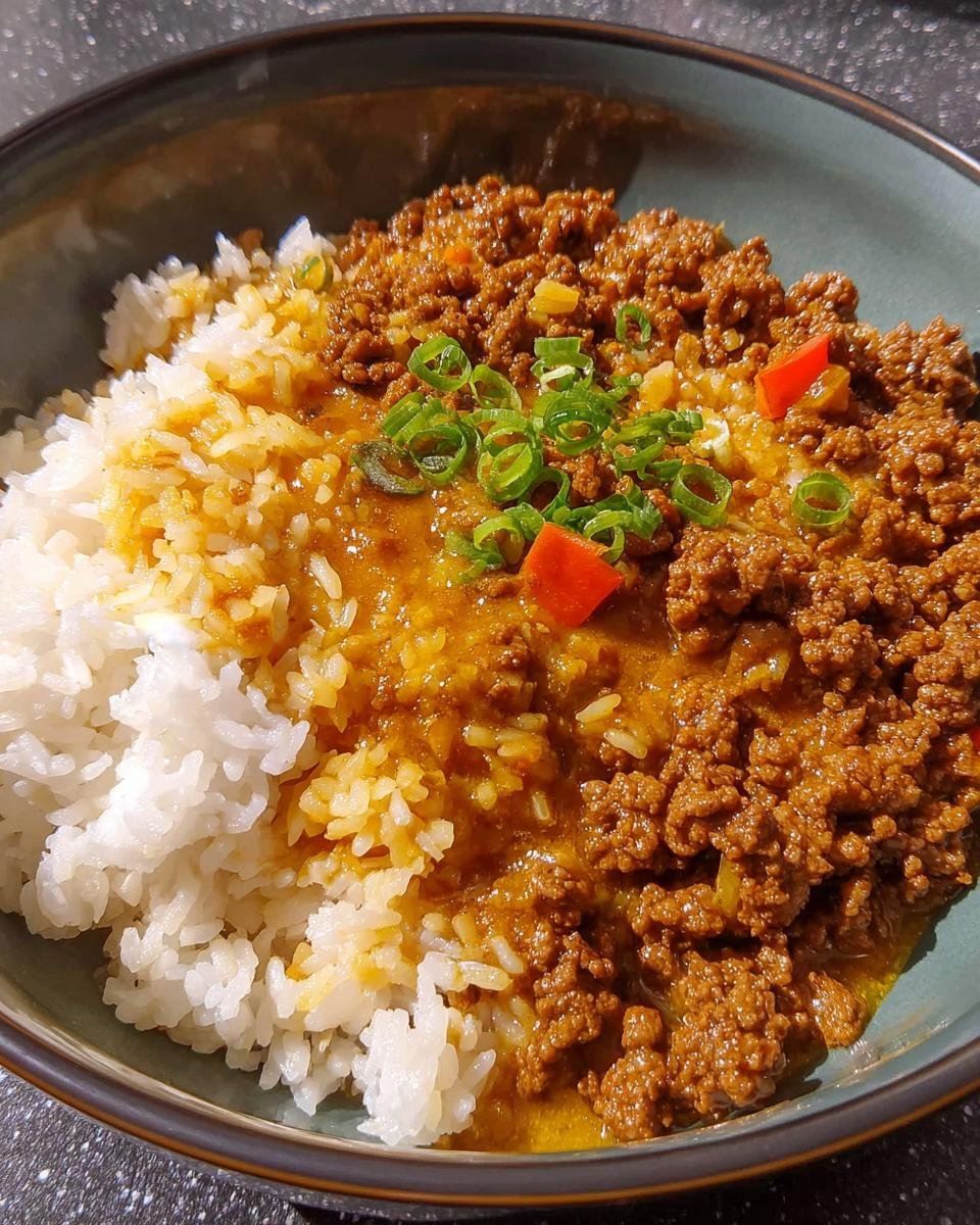 Nahaufnahme von Curryreis mit Hackfleisch, garniert mit Frühlingszwiebeln und Paprika.