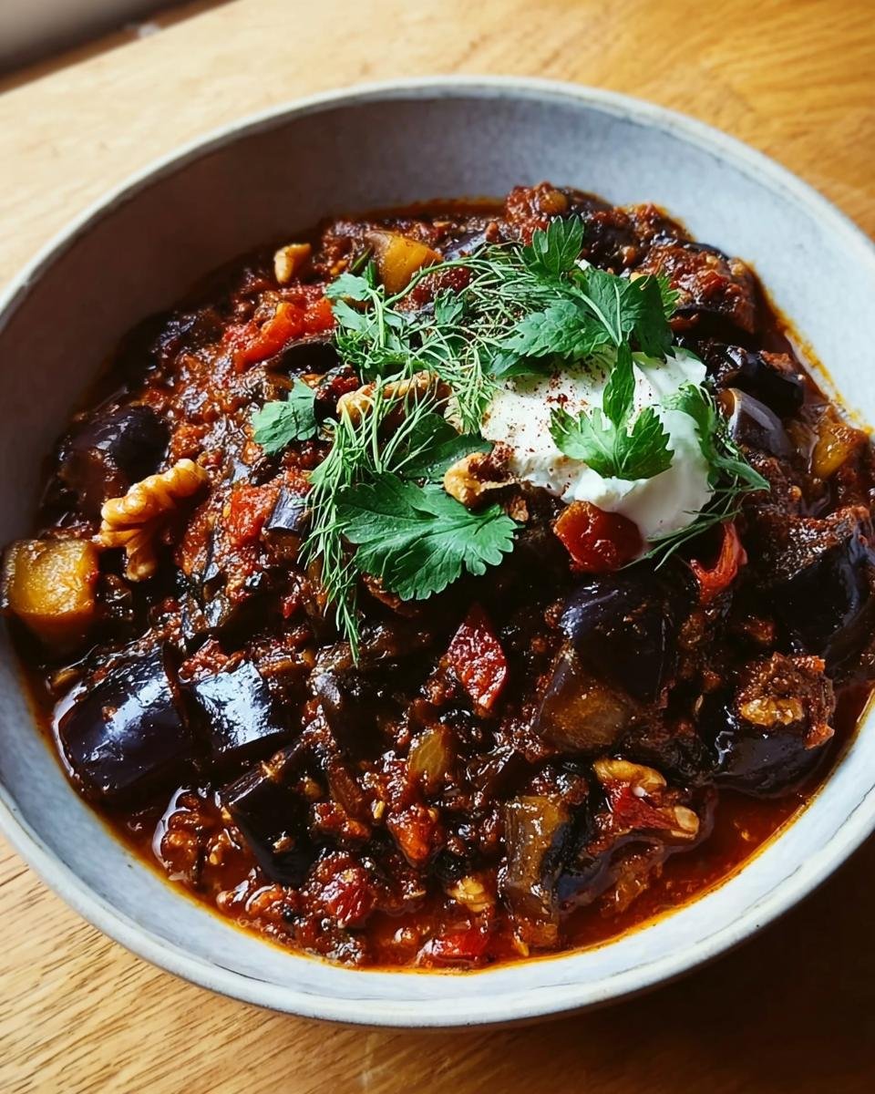 Nahaufnahme des Gewürzte Aubergine & Walnuss-Eintopf, garniert mit Joghurt und frischen Kräutern.