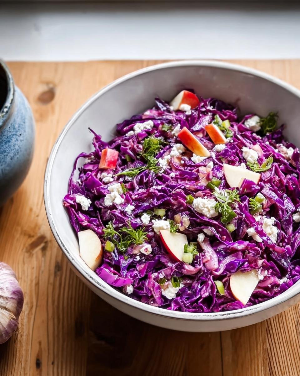 Nahaufnahme einer Schüssel mit frischem Rotkohlsalat mit Apfel und Feta, garniert mit Kräutern.
