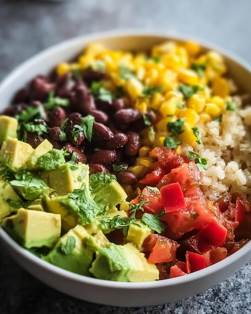 Nahaufnahme einer Schüssel mit Burrito-Bowl mit Reis, Bohnen & Avocado, Mais und gewürfelten Tomaten.